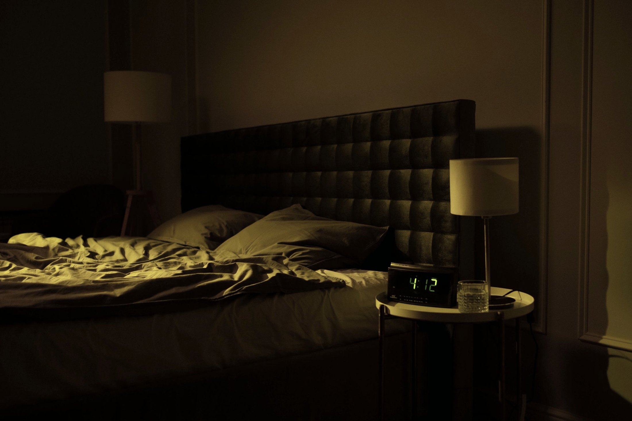 An unmade, empty bed at 4am with the bedside lamp still on